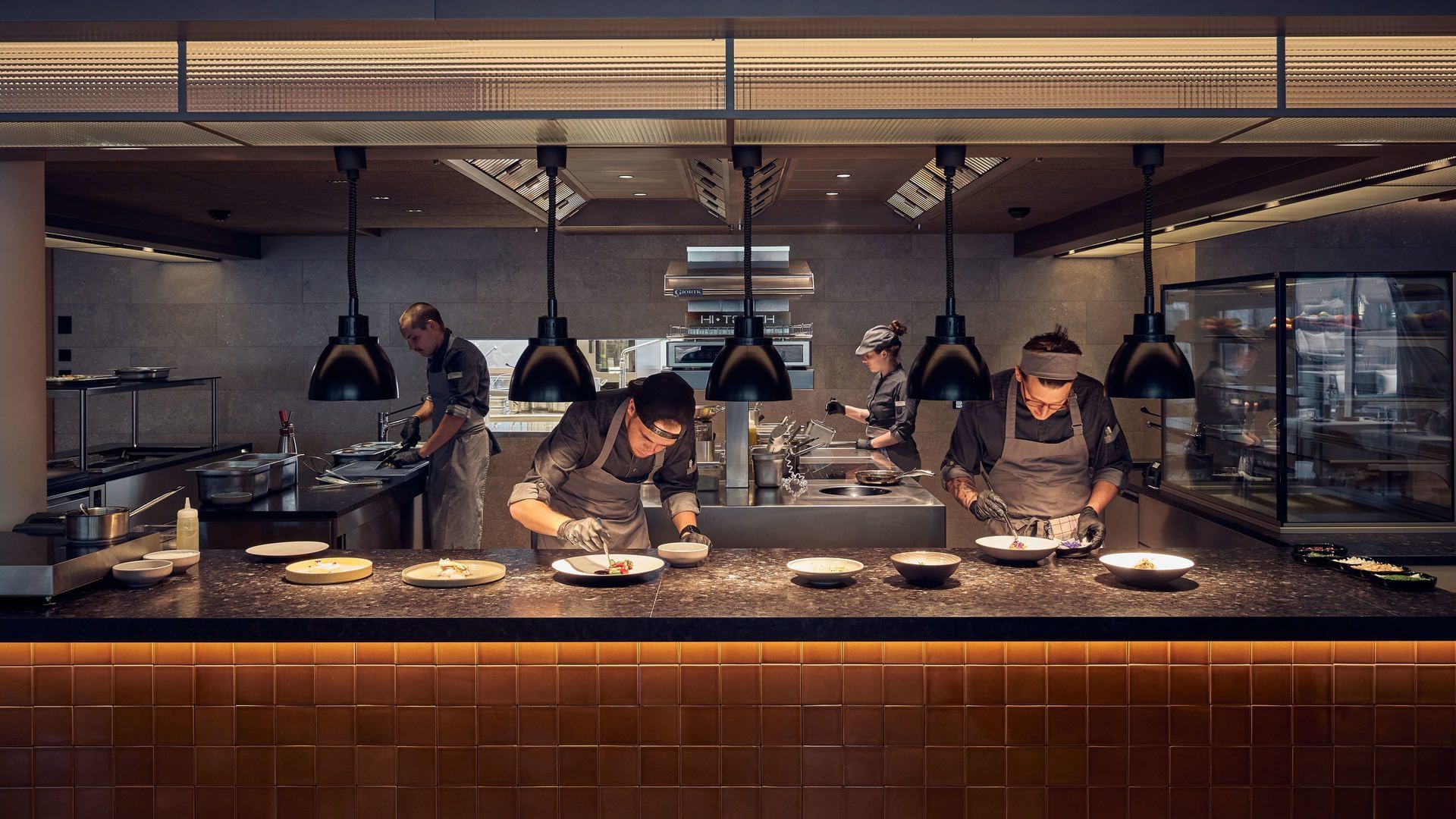 Chefs in a kitchen preparing dishes on a counter at Falkensteiner Hotel Kronplatz