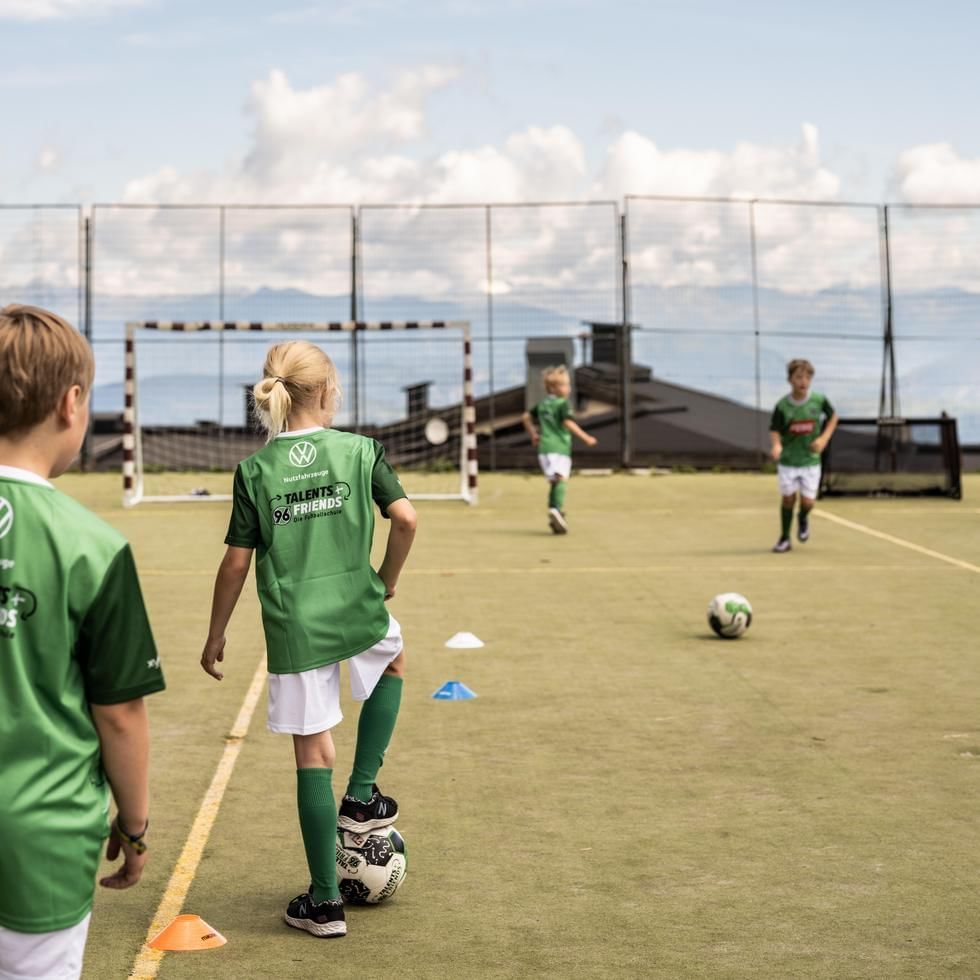 Children in green jerseys playing soccer on an outdoor field at Falkensteiner Hotel & Spa Jesolo