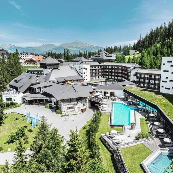 Aerial view of a resort with two pools, surrounded by trees and mountains in the background.
