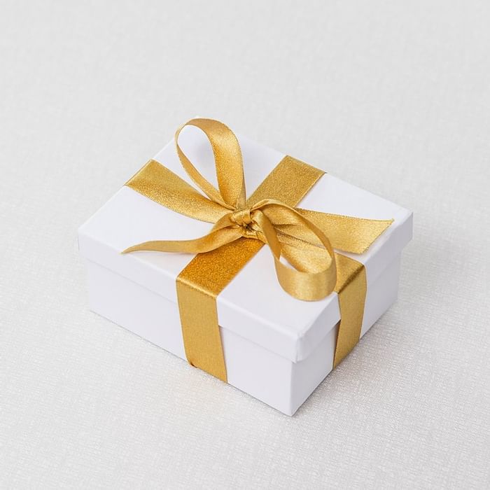A gift box tied with a golden ribbon on a light background at Falkensteiner Hotels & Residences