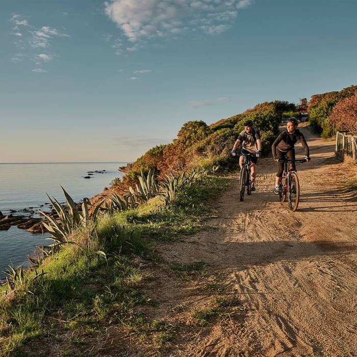 Two cyclists on a dirt road amidst lush green hills at Falkensteiner Hotels & Residences