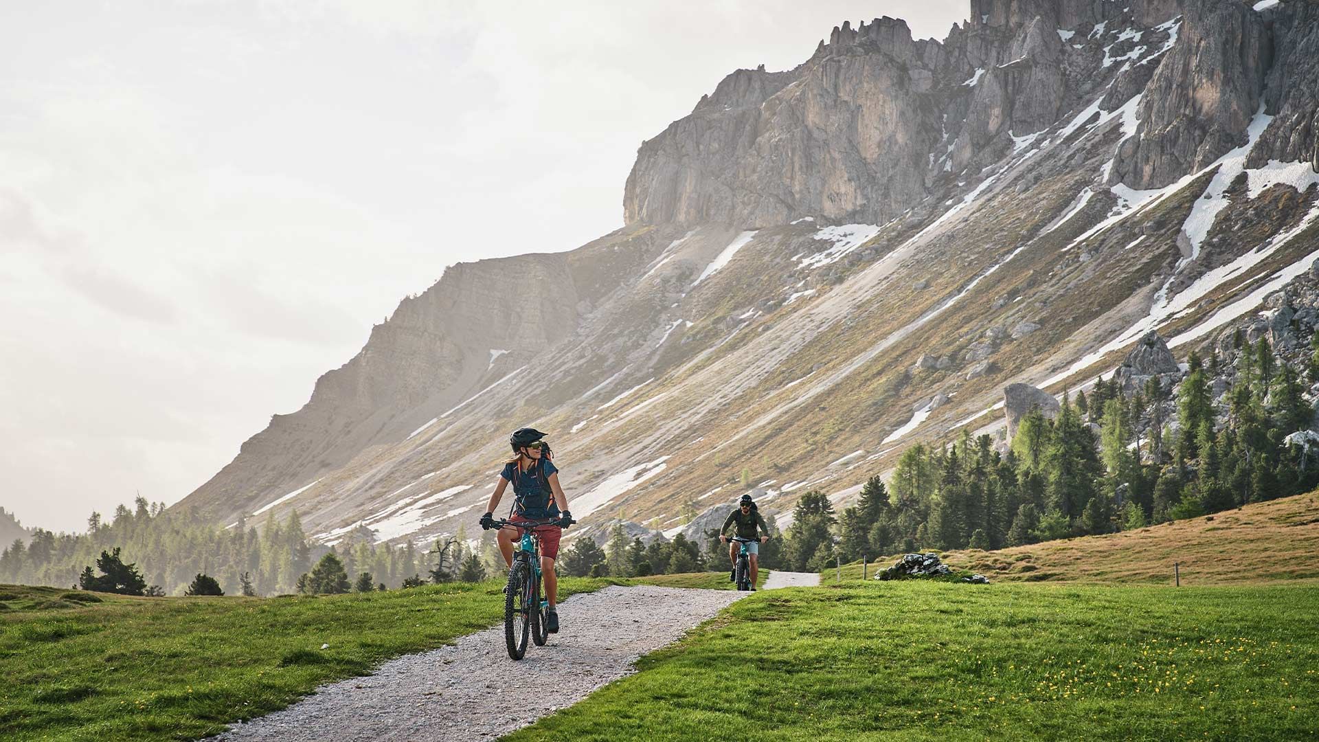 Two cyclists on a mountain trail with scenic rocky peaks in the background at Falkensteiner Hotels & Residences