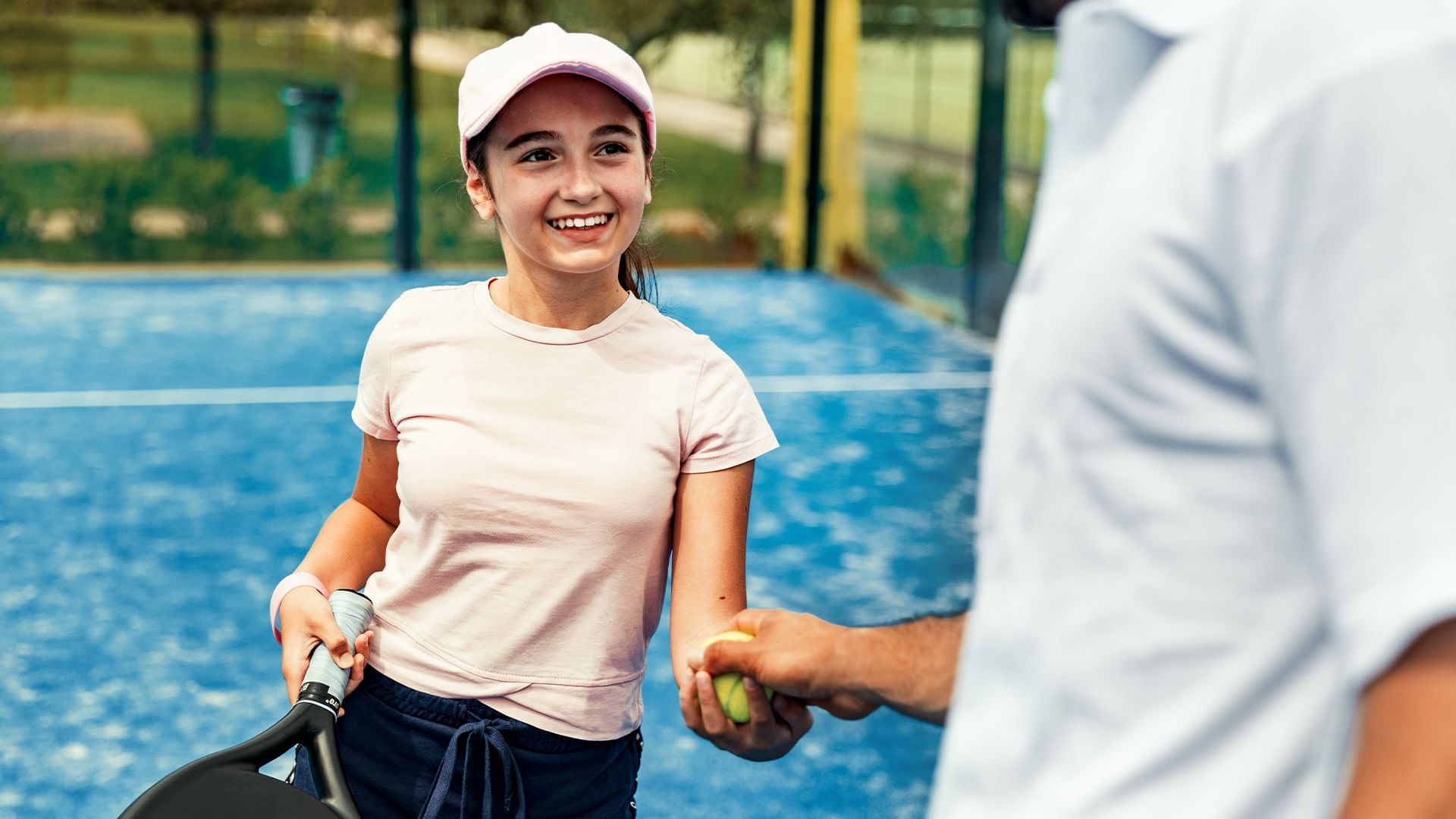 A woman holding a tennis racket receives a ball from a man on a tennis court.