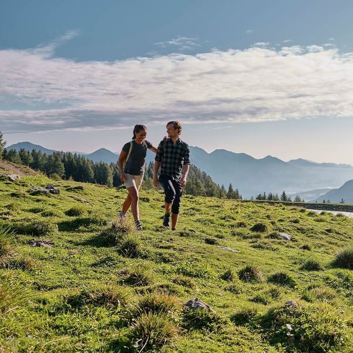 A couple walking in a grassy mountain valley near Falkensteiner Hotels & Residences