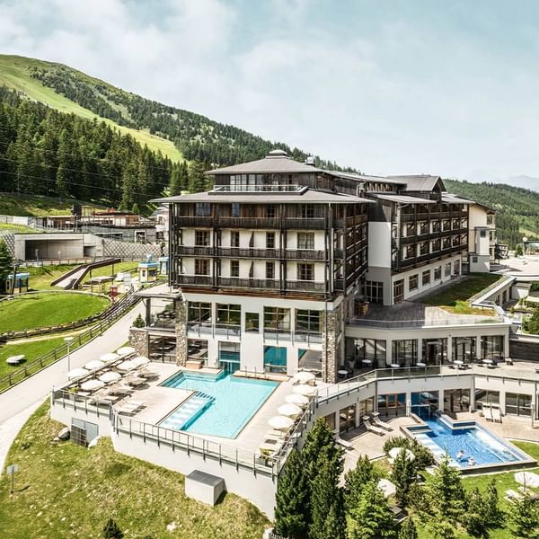 Hotel exterior with outdoor pools amidst lush green hills at Falkensteiner Hotel Cristallo Katschberg