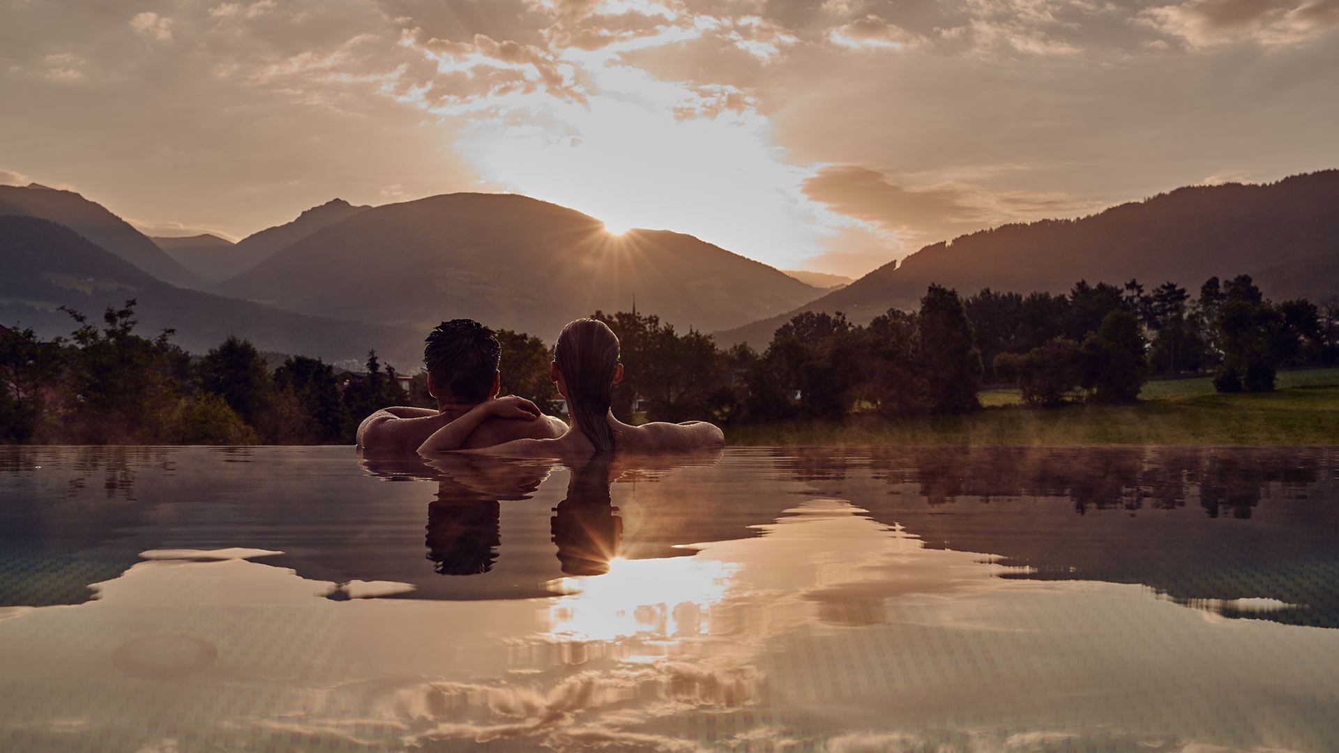 Couple relaxing in a pool overlooking the sunset by mountains at Falkensteiner Hotel Kronplatz