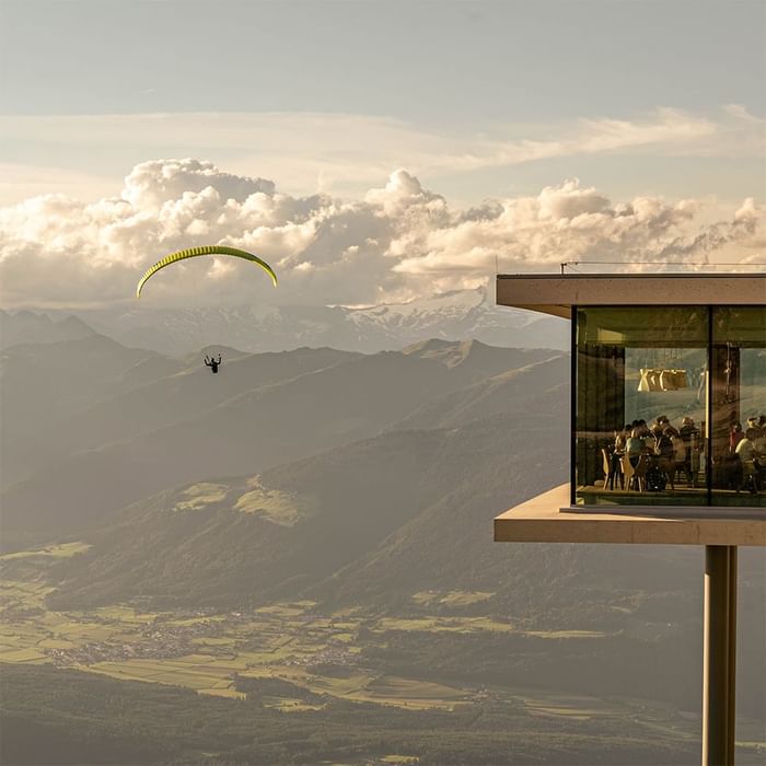 Paraglider flying near a mountain view platform with people near Falkensteiner Hotel Kronplatz