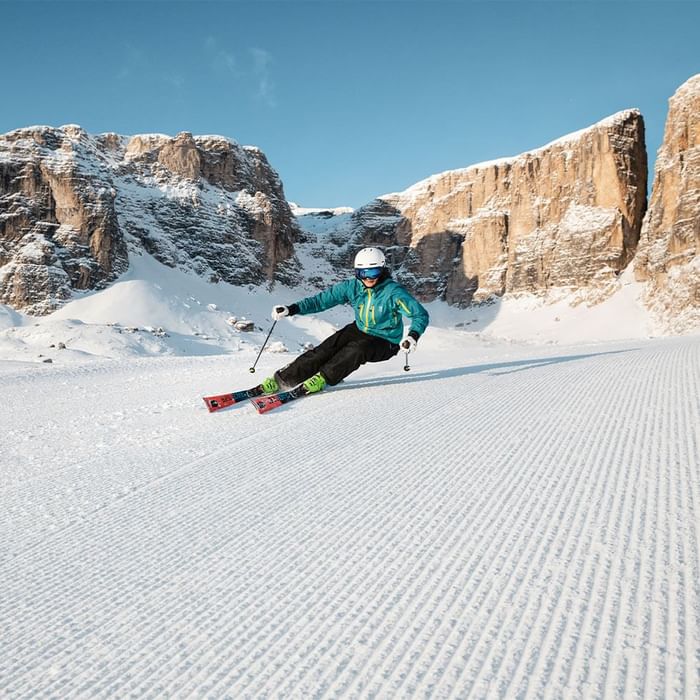 Skier carving on a slope with rocky mountains in background at Falkensteiner Hotel Kronplatz