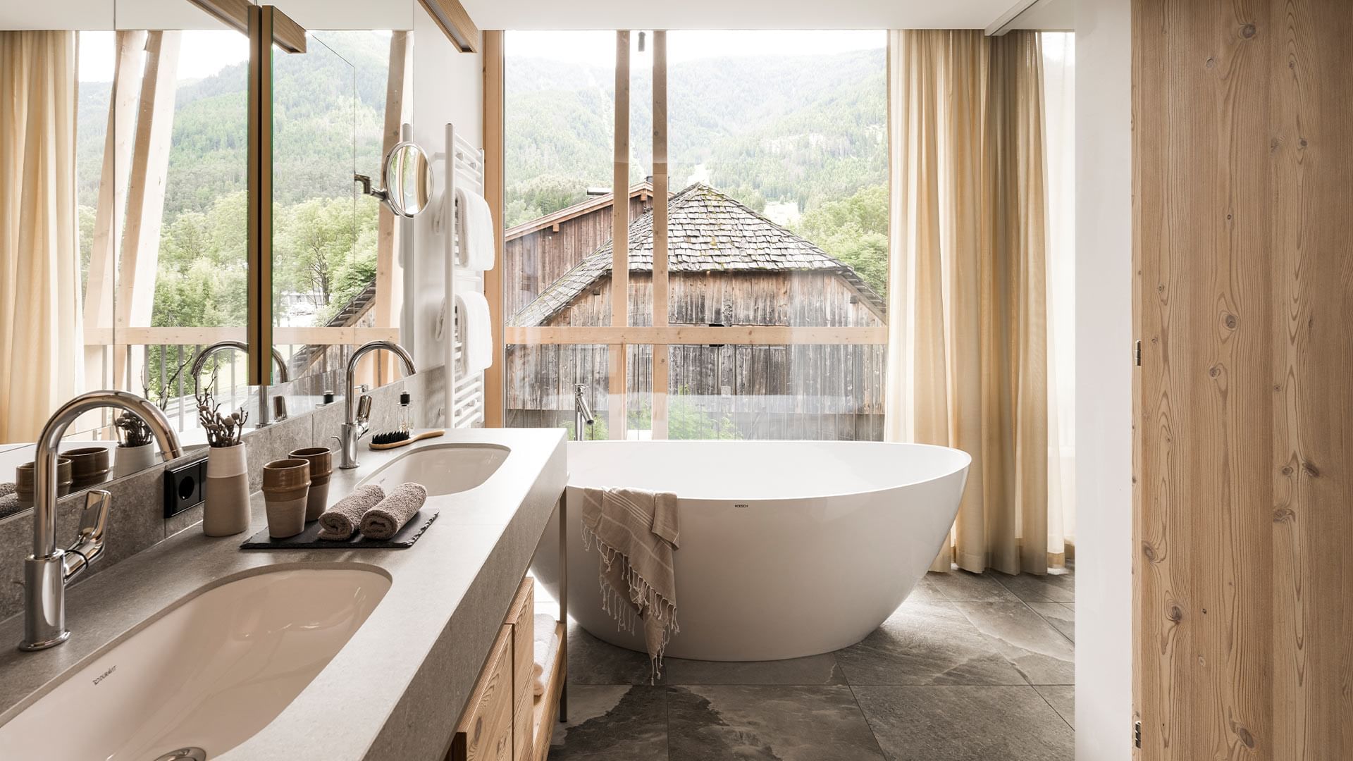 Bathroom of Summit Suite with a bathtub and a mountain view through windows at Falkensteiner Hotel Kronplatz