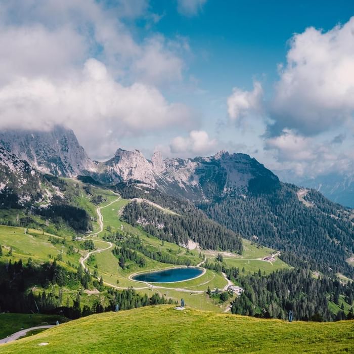 Panorama di montagne verdi e boscose con un lago centrale sotto un cielo blu parzialmente nuvoloso.