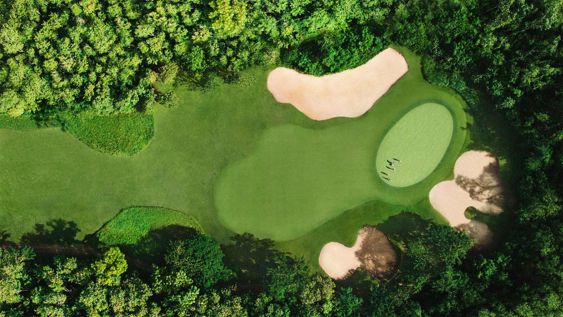 An aerial view of a golf course with green fairways, sand bunkers, and a group of people on the putting green.