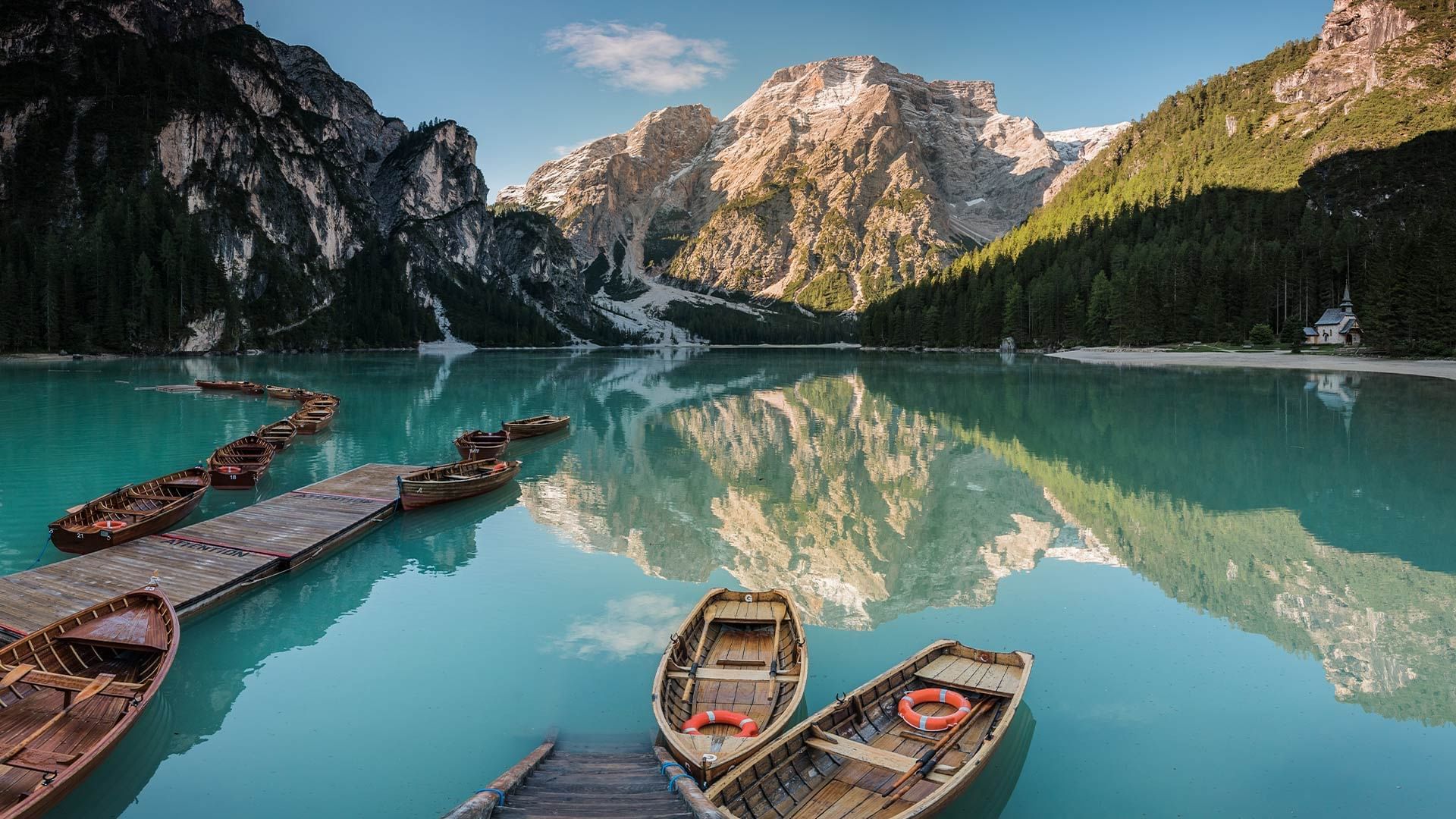 Rowboats on a lake with a dock, mountains in the background, and a reflection of the sky and mountains.