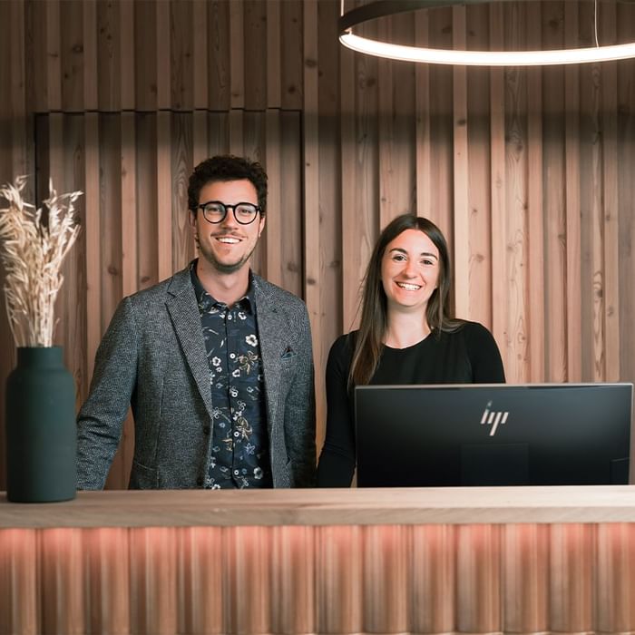 Two receptionists standing behind a front desk with a computer at Falkensteiner Hotels & Residences