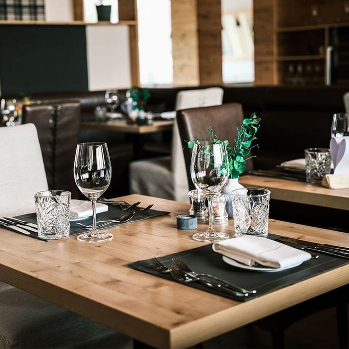 Elegant eingerichtetes Restaurant mit Holztischen, weißen Stühlen, Gläsern und Besteck.