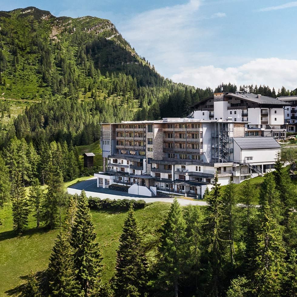 Modern hotel amidst lush greenery with mountains in the background at Falkensteiner Hotel Sonnenalpe