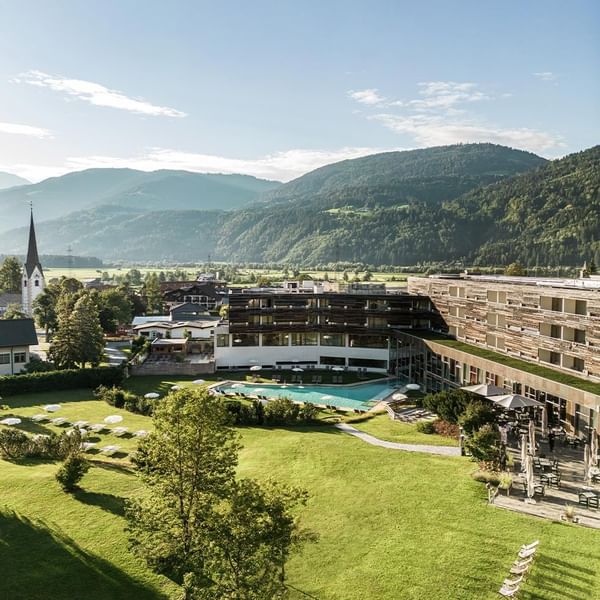 Distance view of hotel with outdoor pools amidst lush green hills at Falkensteiner Hotel & Spa Carinzia