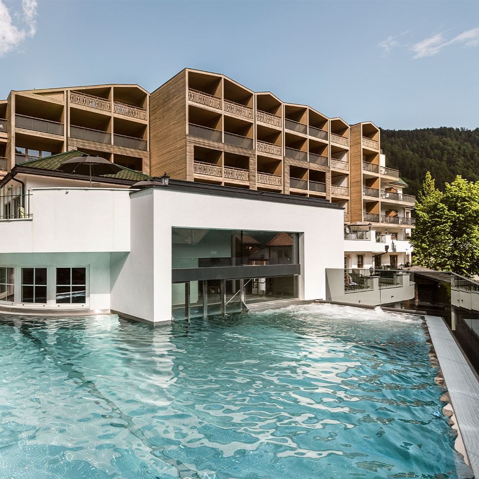 Hotel exterior with an outdoor pool set against a mountainous backdrop at Falkensteiner Hotel & SPA Falkensteinerhof
