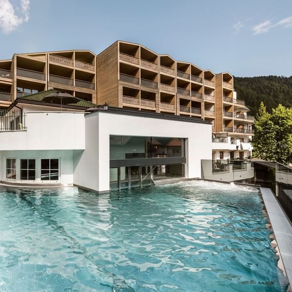 Hotel exterior with an outdoor pool set against a mountainous backdrop at Falkensteiner Hotel & SPA Falkensteinerhof