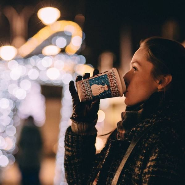 Eine Frau trinkt aus einem festlichen Becher vor einem leuchtenden Hintergrund in der Nacht.