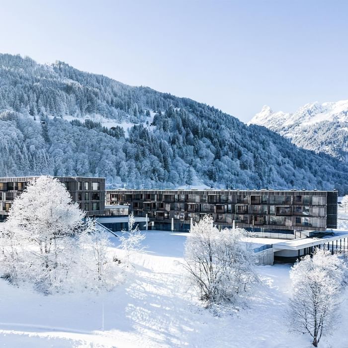 Exterior view of snow-covered Falkensteiner Hotel Montafon with forested hill backdrop