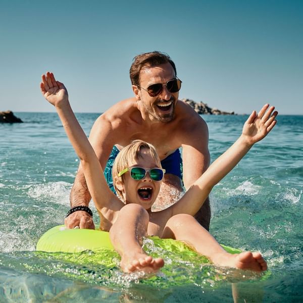 Dad and son playing on a float in the sea near Falkensteiner Resort Capo Boi