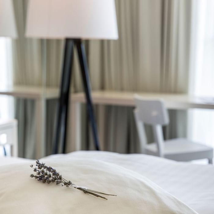 Close-up of a lavender on a neatly made bed by a working table at Falkensteiner Hotels & Residences