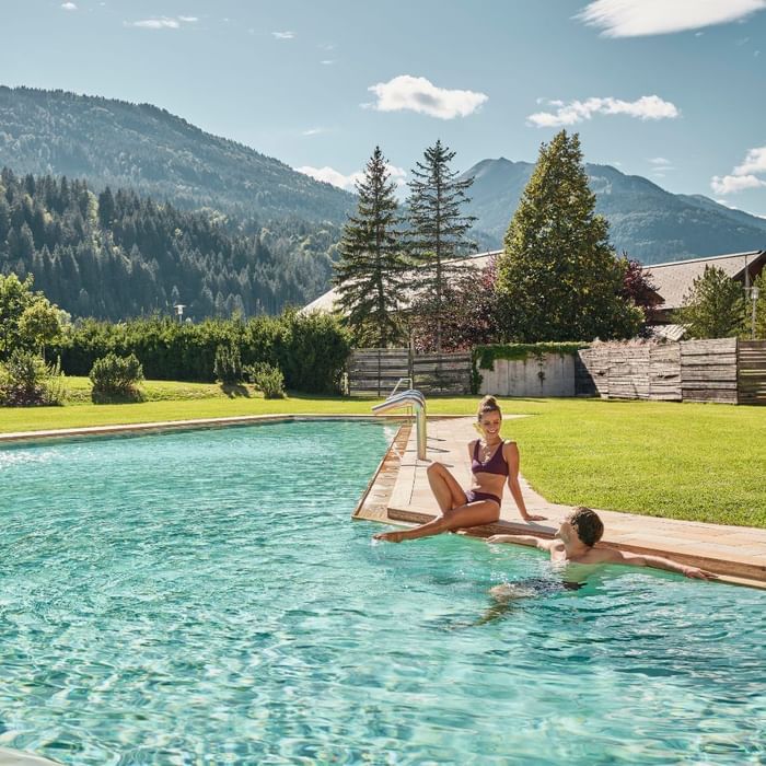 Una donna e un uomo si rilassano in piscina con vista sulle montagne e verde circostante.