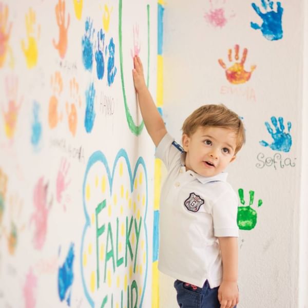 A kid keeping hand prints on the white wall at Falkensteiner Hotels & Residences