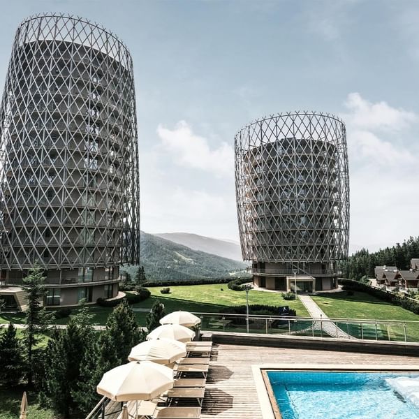 Two cylindrical patterned towers beside a pool with lounge chairs at Falkensteiner Hotels & Residences