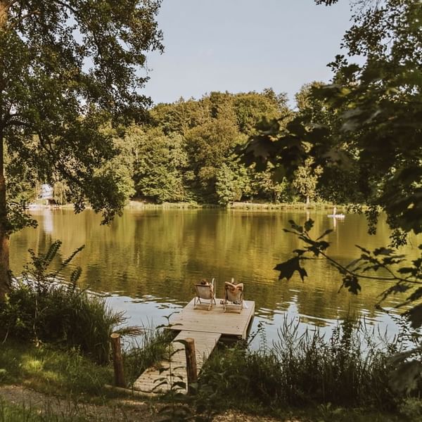 Two people relax on a wooden dock by a lake, surrounded by lush greenery near Falkensteiner Hotels & Residences