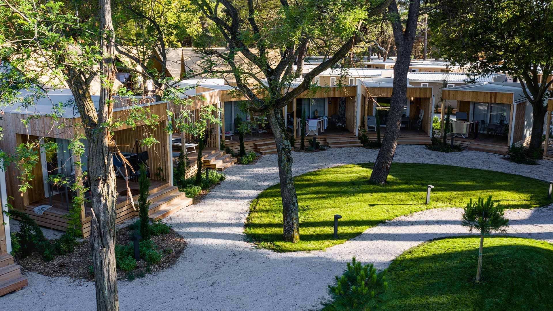 Modern wooden cabins surrounded by a path and lush green landscaping at Falkensteiner Hotels & Residences