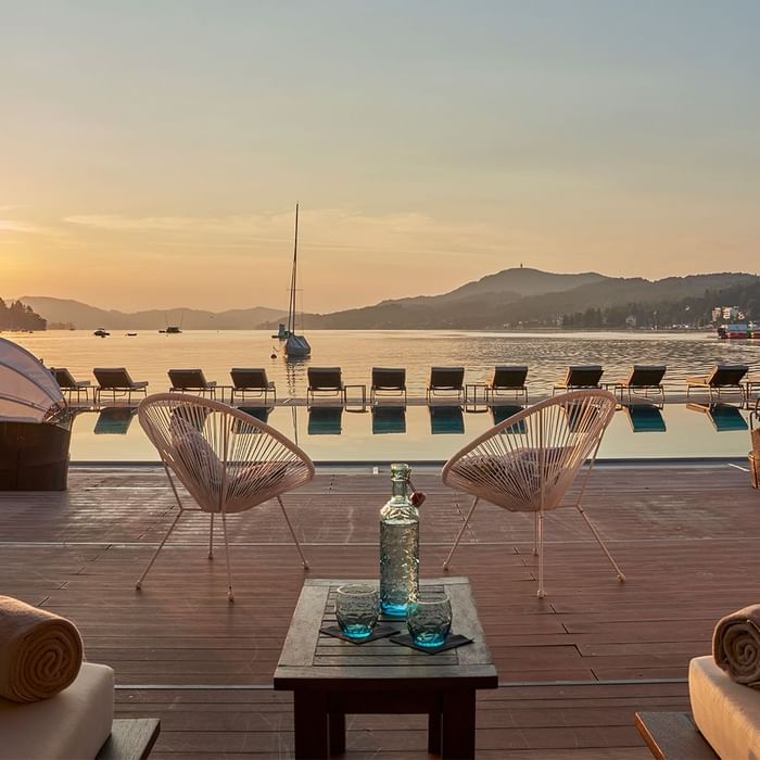 Outdoor lounge area with chairs, table, and water view at sunset.