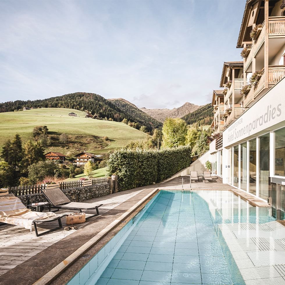 Outdoor pool area with lounges and mountain backdrop at Falkensteiner Hotels & Residences
