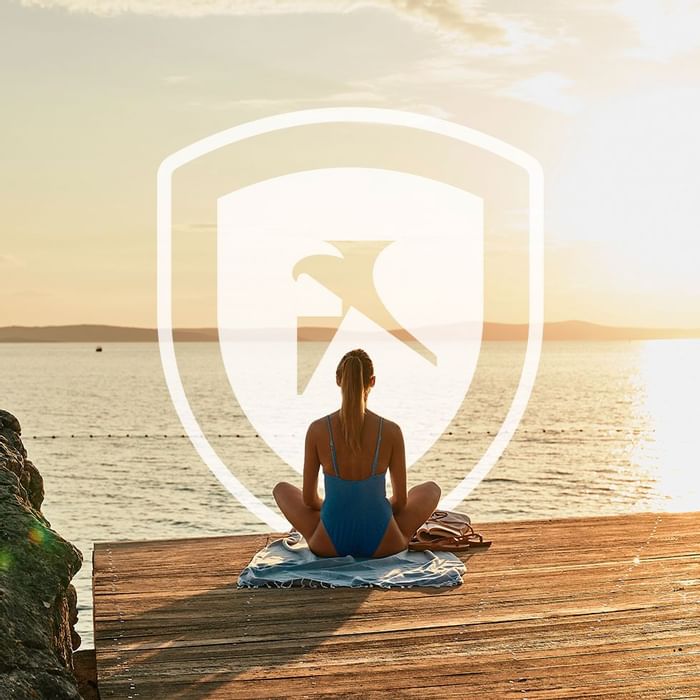 Woman meditating on a dock with a digital security shield icon overlaid at Falkensteiner Hotels & Residences