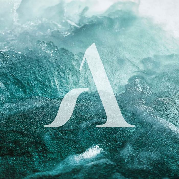 A stylized letter 'A' overlaid on an image of turbulent sea waves at Falkensteiner Hotels & Residences